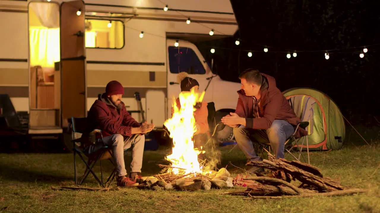 Friends warming up their hands during a cold night at camp fire