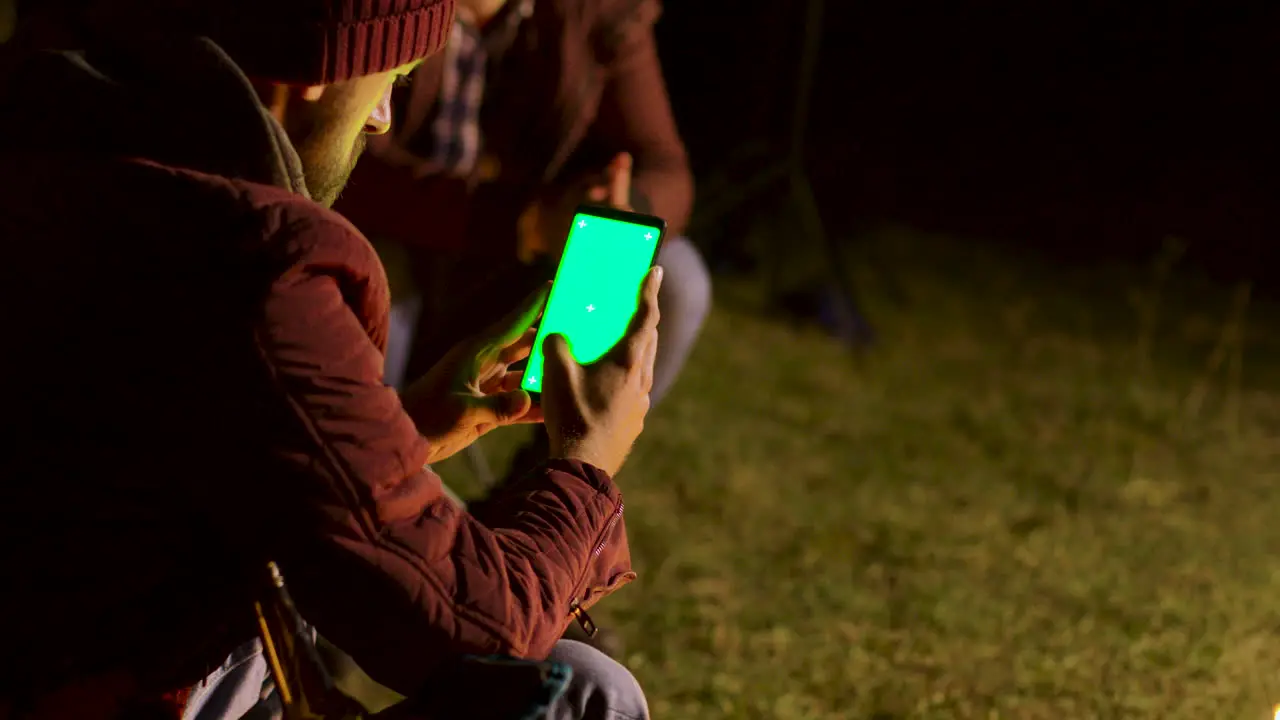 Tourist scorlling down on phone with green screen around camp fire