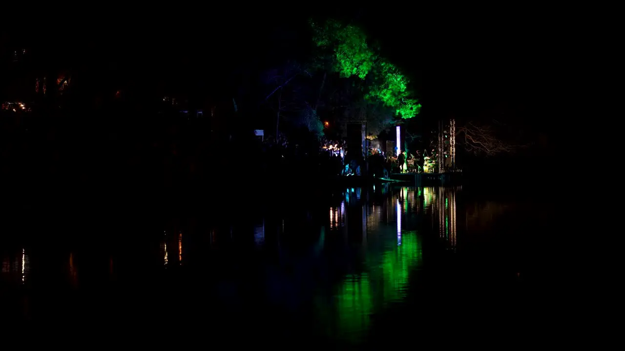 Multicolored lights at night live concert singer with music group perform near city park lake