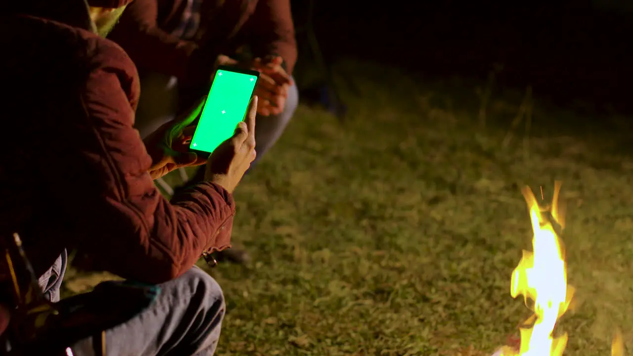 Man looking at this phone with green screen around camp fire