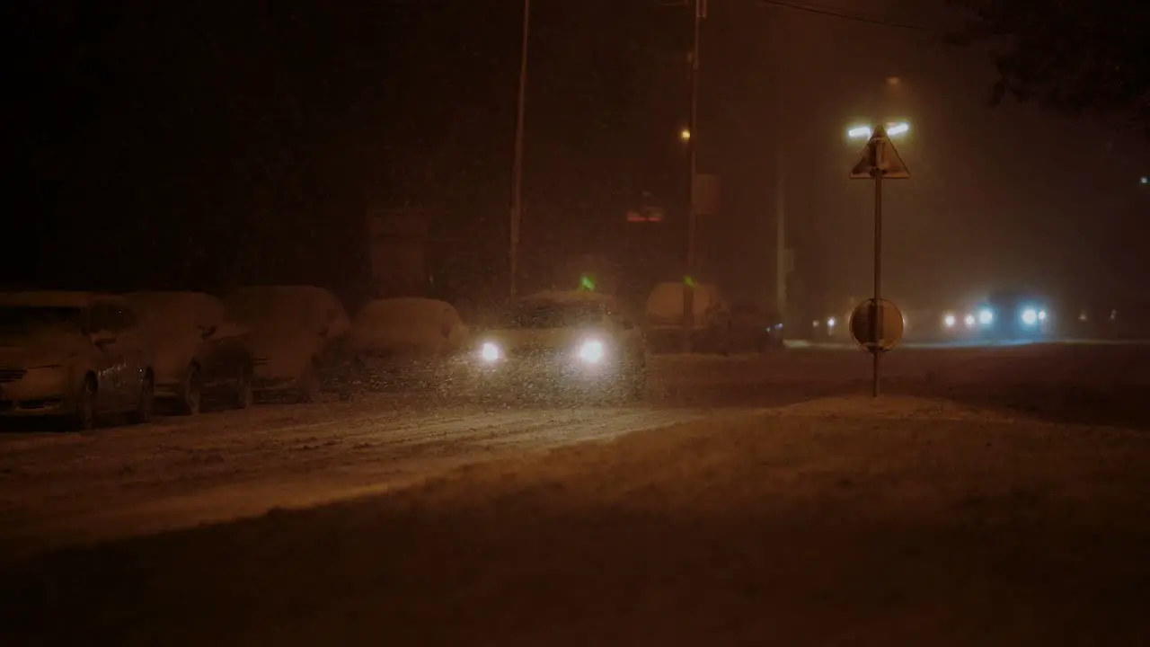 Lone car driving in the city on a frosty winter night during a blizzard warm lights