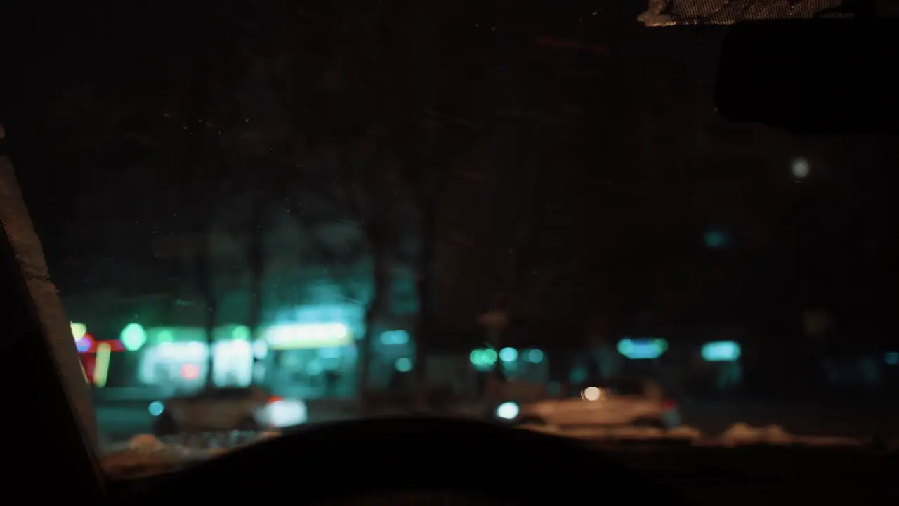 Inside a car during a frosty winter night in the city wipers on