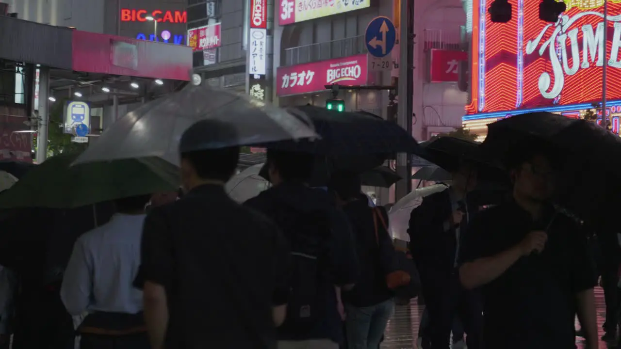 Many local people walk through a rainy tokyo at night with many lights in the background