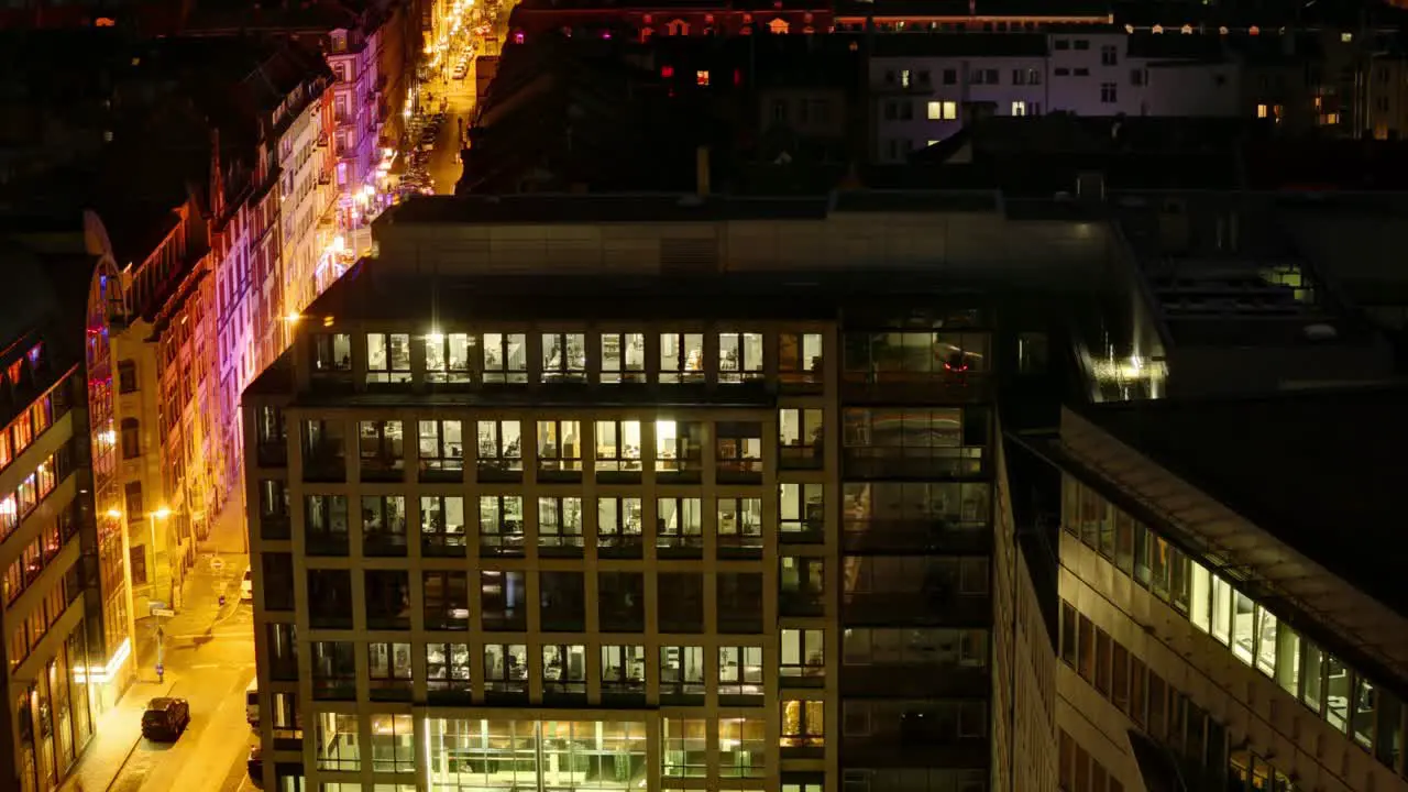 This timelapse presents a vibrant urban nightscape viewed from a high angle showcasing modern buildings with numerous lit windows and orange streetlights lining the streets