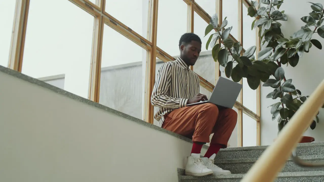 Hombre Afro Sentado En Un Edificio Moderno Y Trabajando En Una Laptop