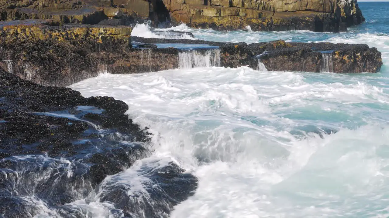 Seawater streaming down face of rocks on coastline covered with small black mussels