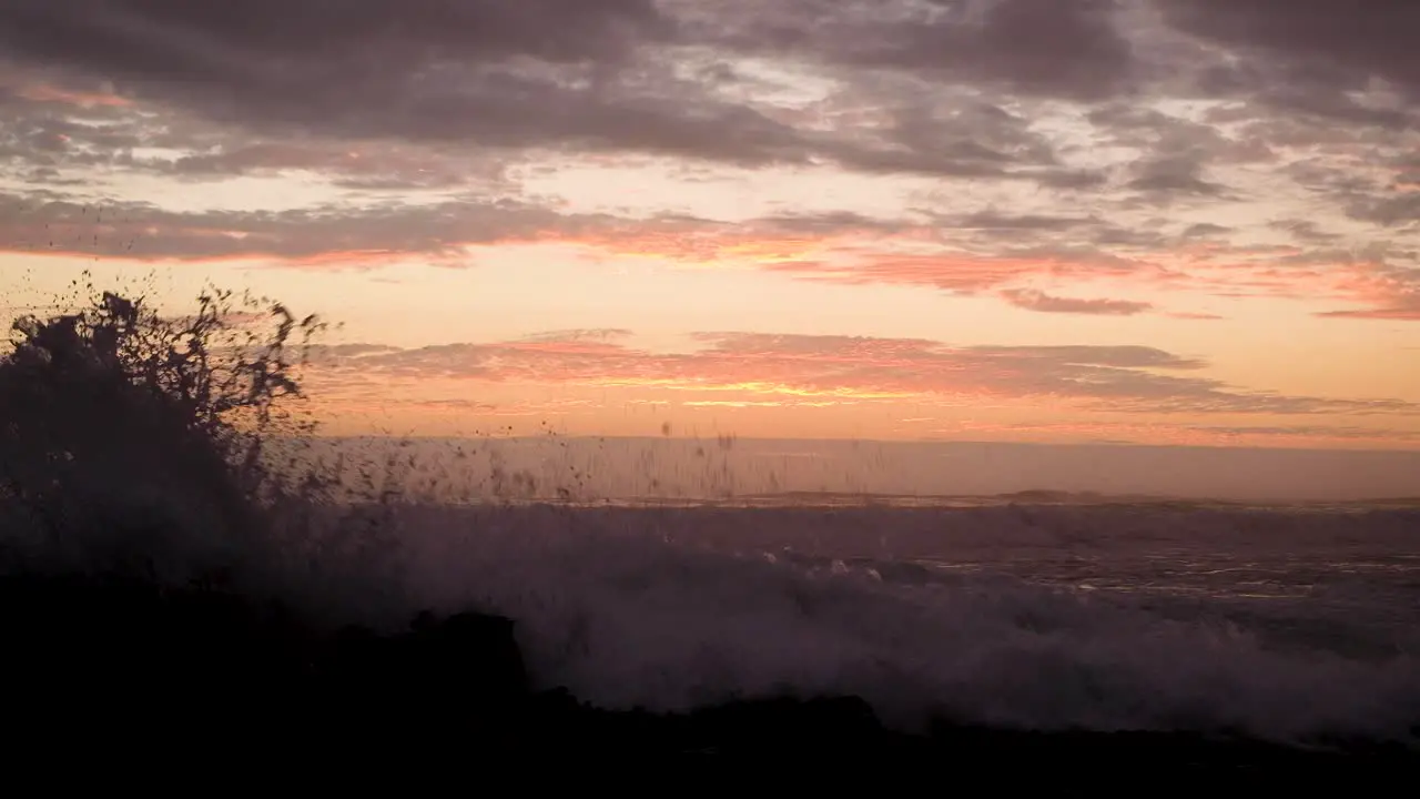 Rough Atlantic ocean waves crashing against rocky shore with orange sunset