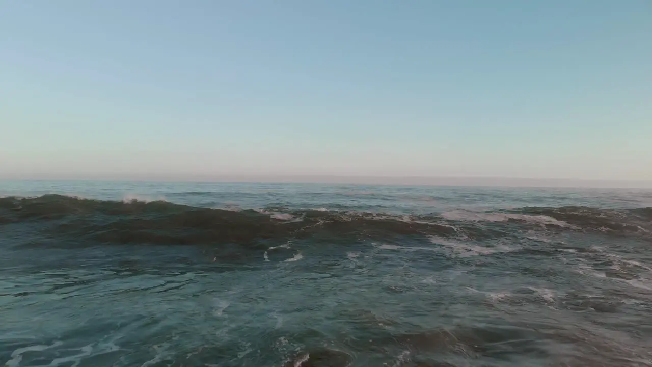 Drone flying low over open waters with bamboo floating on the surface as swells and waves come in and break