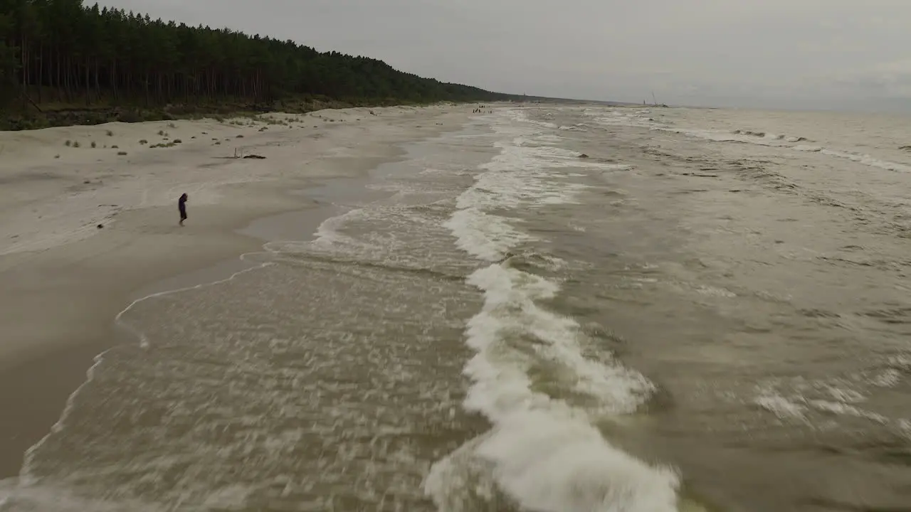 Drone shot of beach and Baltic Sea flying forward low and fast tilt up and reveal entire beach and one person walking towards the sea on a cloudy day