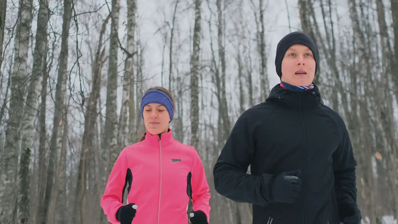 Positive beautiful young healthy couple running with sportswear through the forest in the sunny winter morning