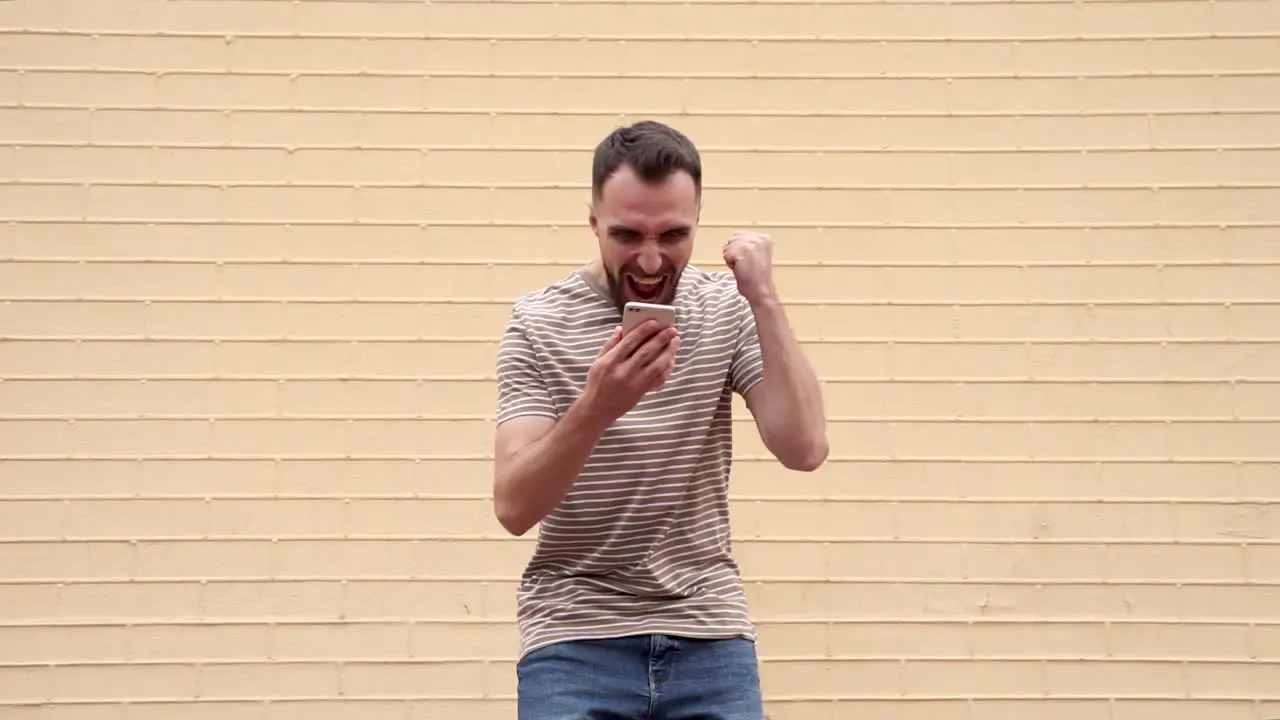 Young Excited Man Overjoyed Looking At The Phone And Celebrating Success Outdoors