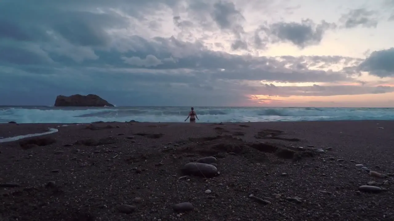 A woman having a swim in the wild sea during sunset