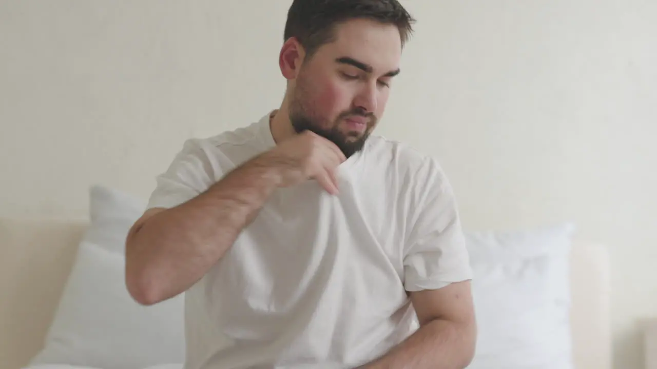 Sick Man With Fever Sitting In Bed Taking Temperature With Thermometer