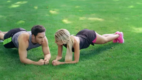 Happy man and woman standing in plank on green grass at fitness training outdoor