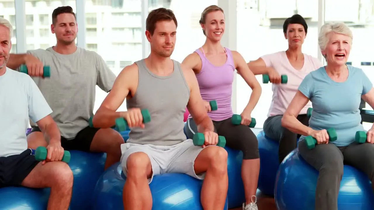 Fitness group sitting on exercise balls lifting hand weights