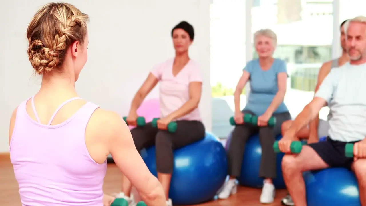 Fitness class sitting on exercise balls lifting hand weights