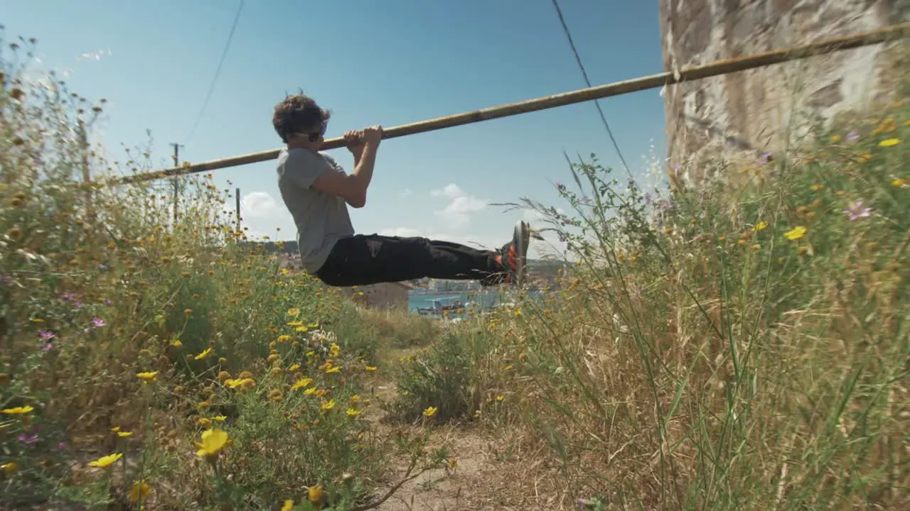 Young fit man does L-sit pull ups street workout using outdoor bar