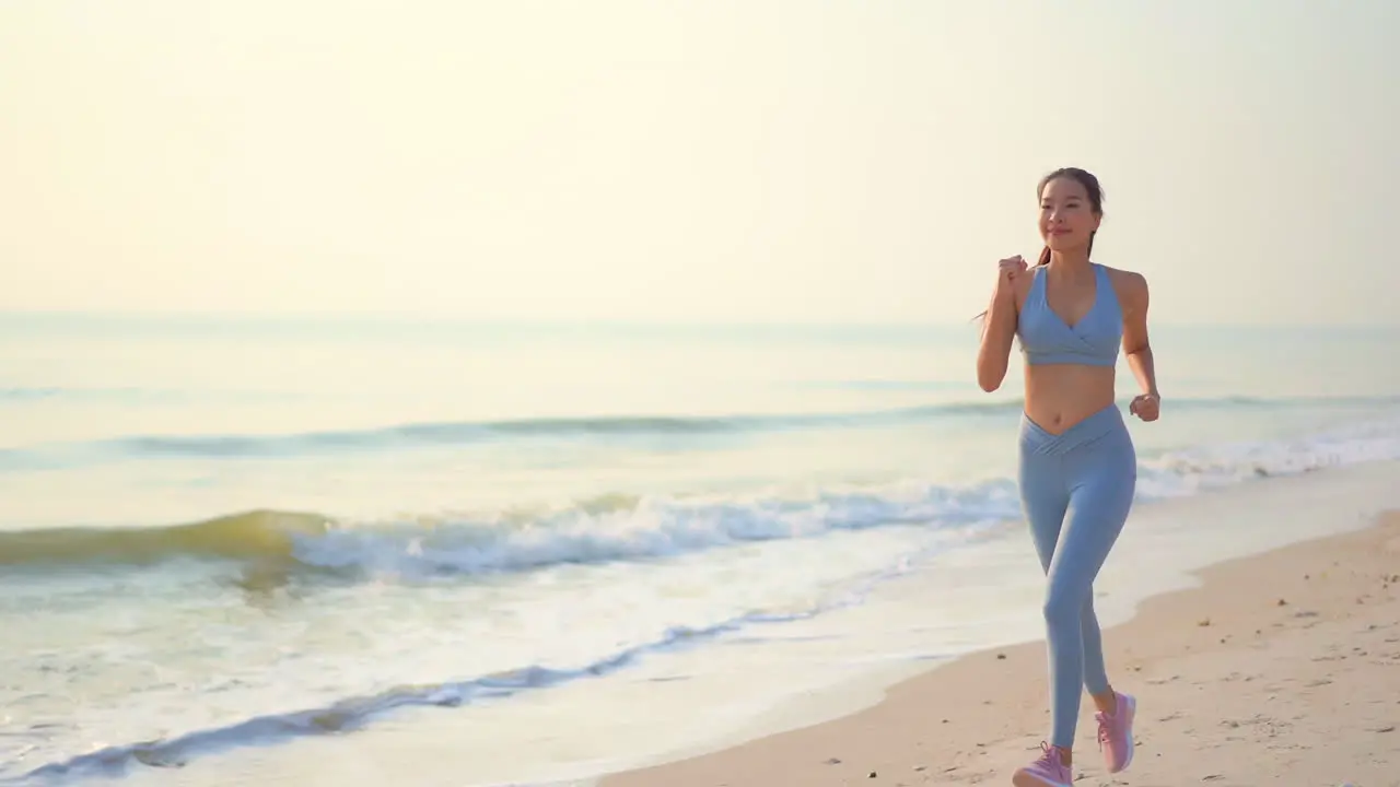 Sporty young Asian girl runner with ponytail at beach towards camera