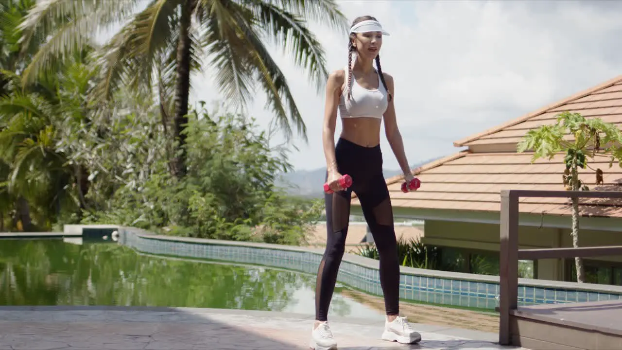 Sportswoman squatting with dumbbells on poolside