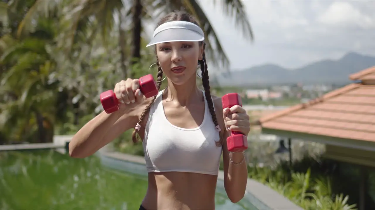 Cheerful woman exercising with dumbbells near swimming pool