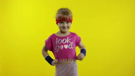 Athletic girl in pink sportswear is waving her hand doing hello gesture on yellow background