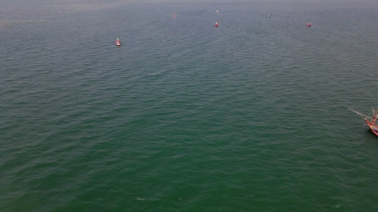 Aerial footage sliding to the left revealing a big fishing boat and more on the top side of the frame as seen in the middle of the ocean in Chonburi Thailand