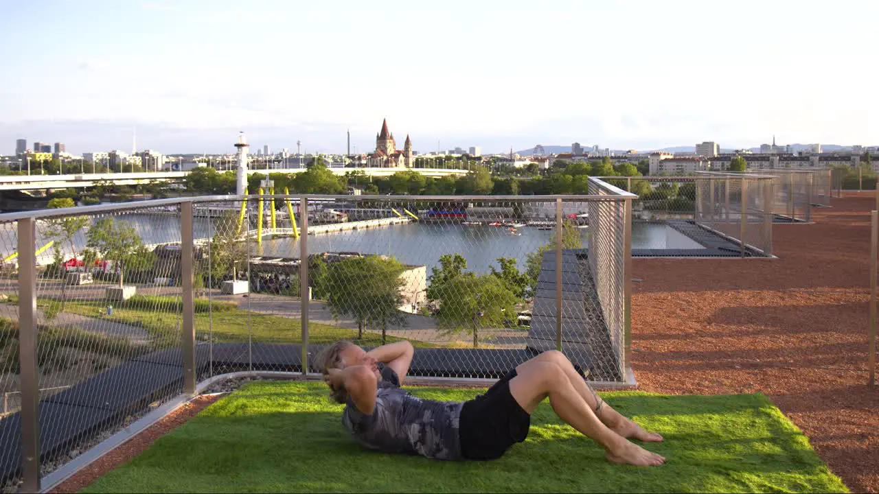 Fitness enthusiast is doing Crunches on a fancy terrace with Boats in the Danube River in the back in Vienna Austria 4K