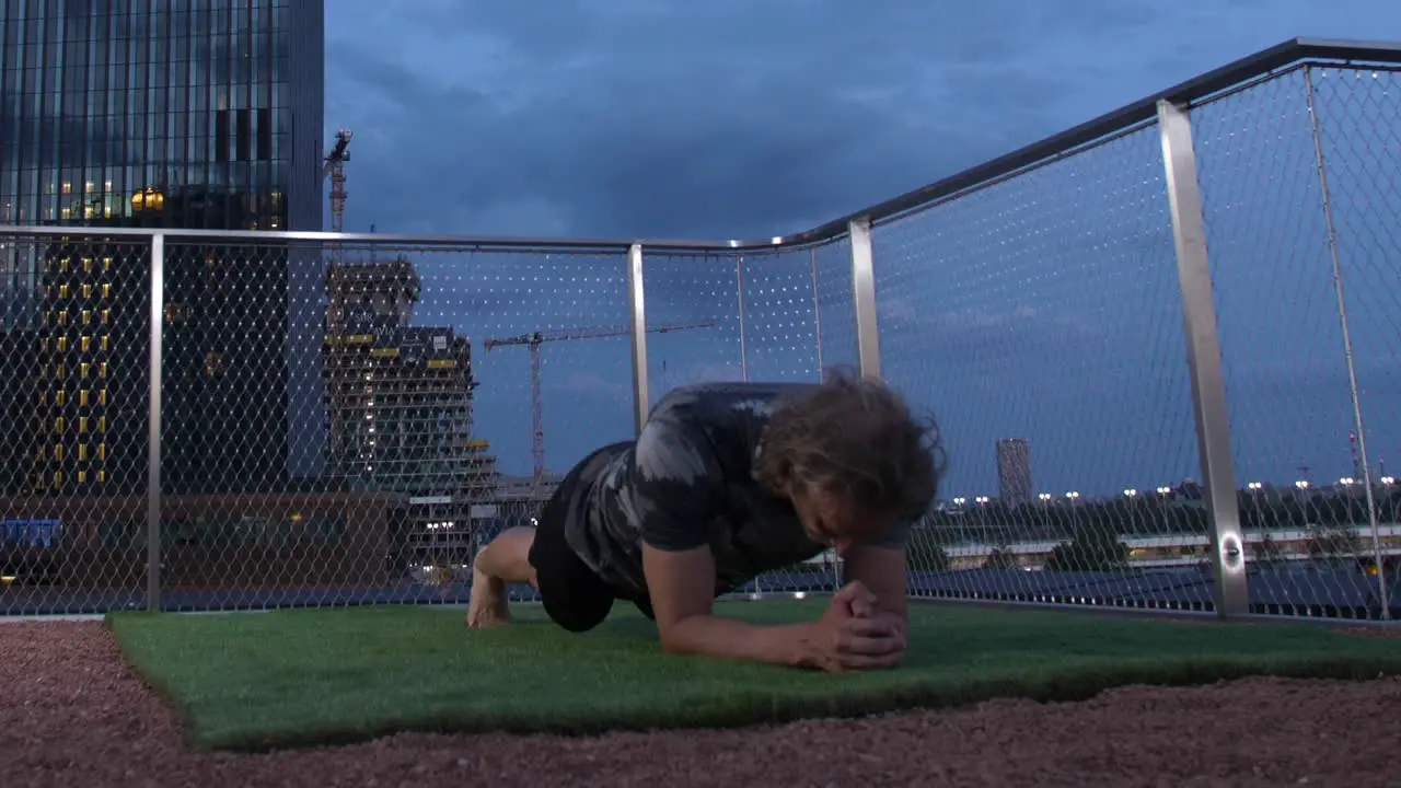 Guy with long hair is doing Plank on a Terrace with the viennese Skyline in the back in the evening 4K Timelapse