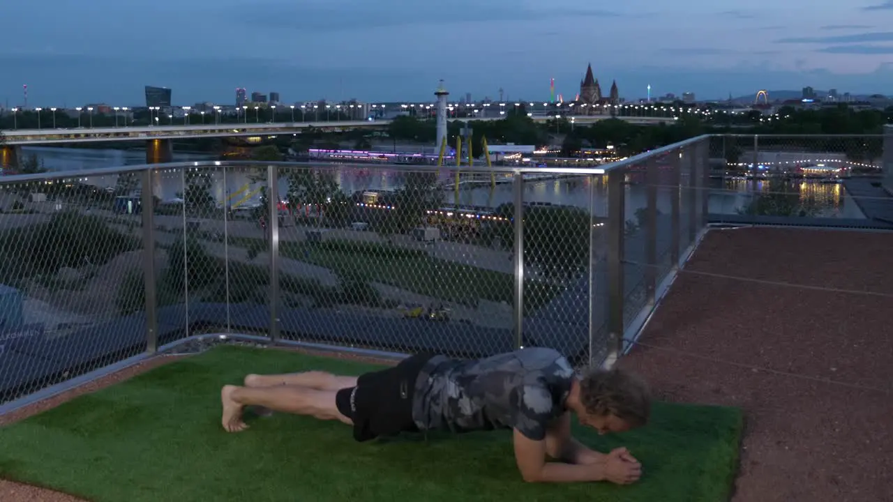 Guy is doing Planks on a Terrace in the evening with the Danube River backdrop in Vienna Austria 4K time lapse