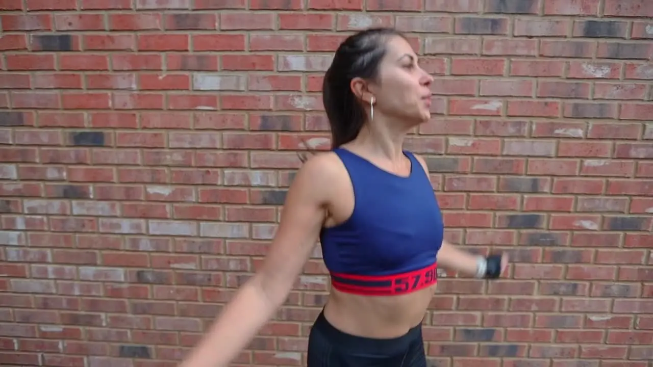 Sporty active Hispanic female doing jumping jacks warm up in front of brick wall