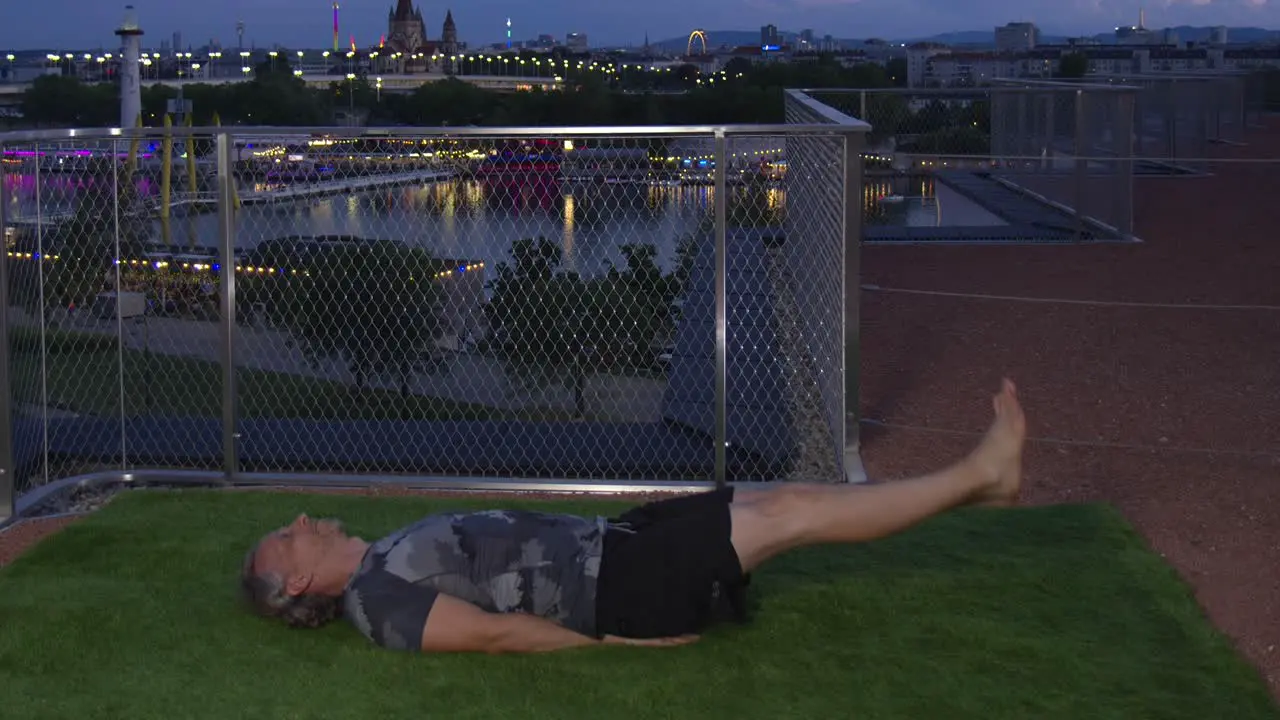 Cool guy is doing Flutter Kicks in the evening on a modern terrace with Danube River backdrop in Vienna 4K Timelapse