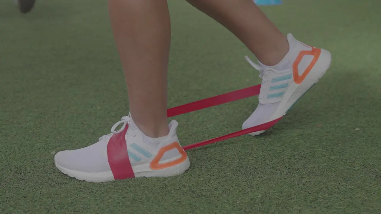 using elastic bands for exercise with feet on green grass and white tennis shoes