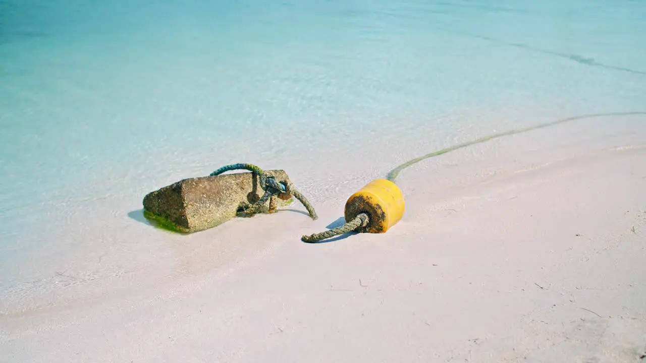 Stone Tied With Thick Rope Used As Anchor Near Yellow Floating Tool On Sandy Beach