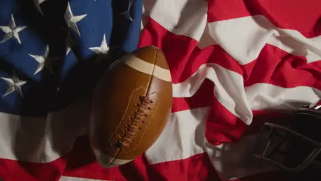 Overhead Shot Of Person Throwing Down American Football Onto Stars And Stripes Flag With Helmet