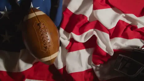 Overhead Shot Of Person Picking Up American Football On Stars And Stripes Flag With Helmet