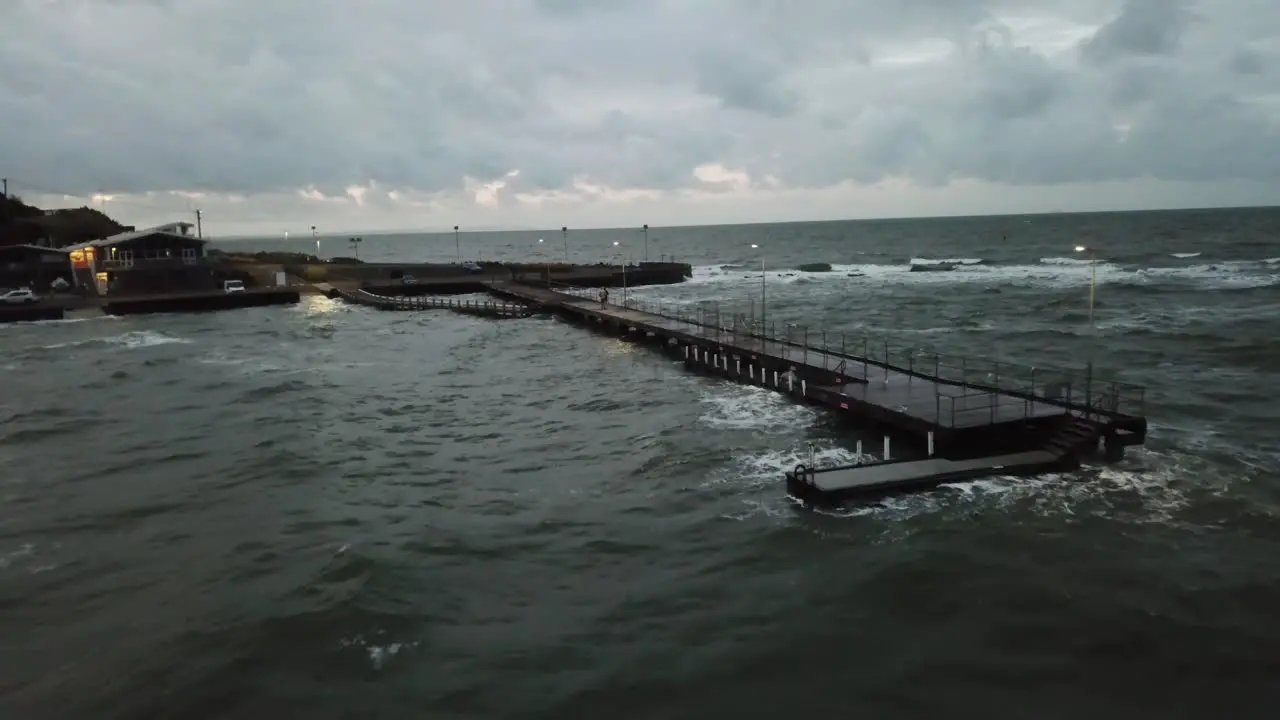 Drone aerial over ocean Melbourne wavy windy cloudy people walking on pier