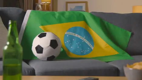 Flag Of Brazil Draped Over Sofa At Home With Football Ready For Match On TV