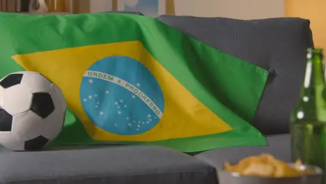 Flag Of Brazil Draped Over Sofa At Home With Football Ready For Match On TV 1