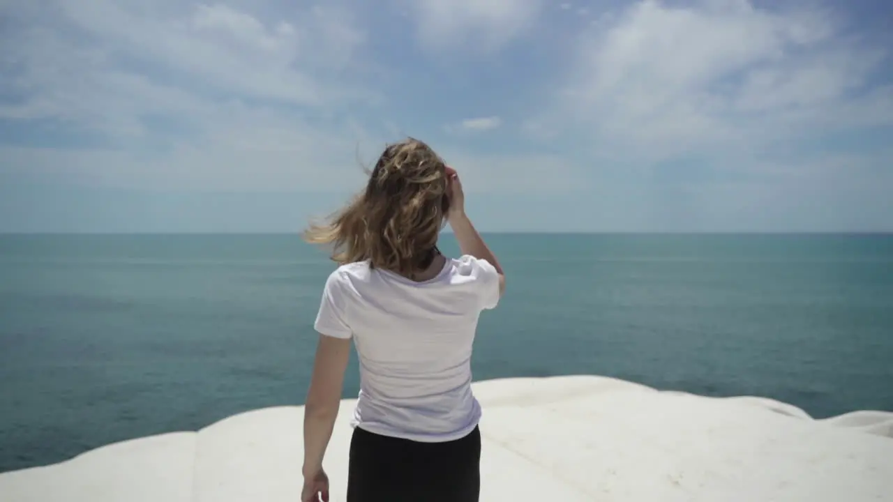 Woman on white rock cliff Scala dei Turchi with view of turquoise blue sea in Sicily