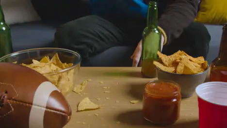 Person At Home Watching American Football Game On TV With Drinks Snacks And Ball 1