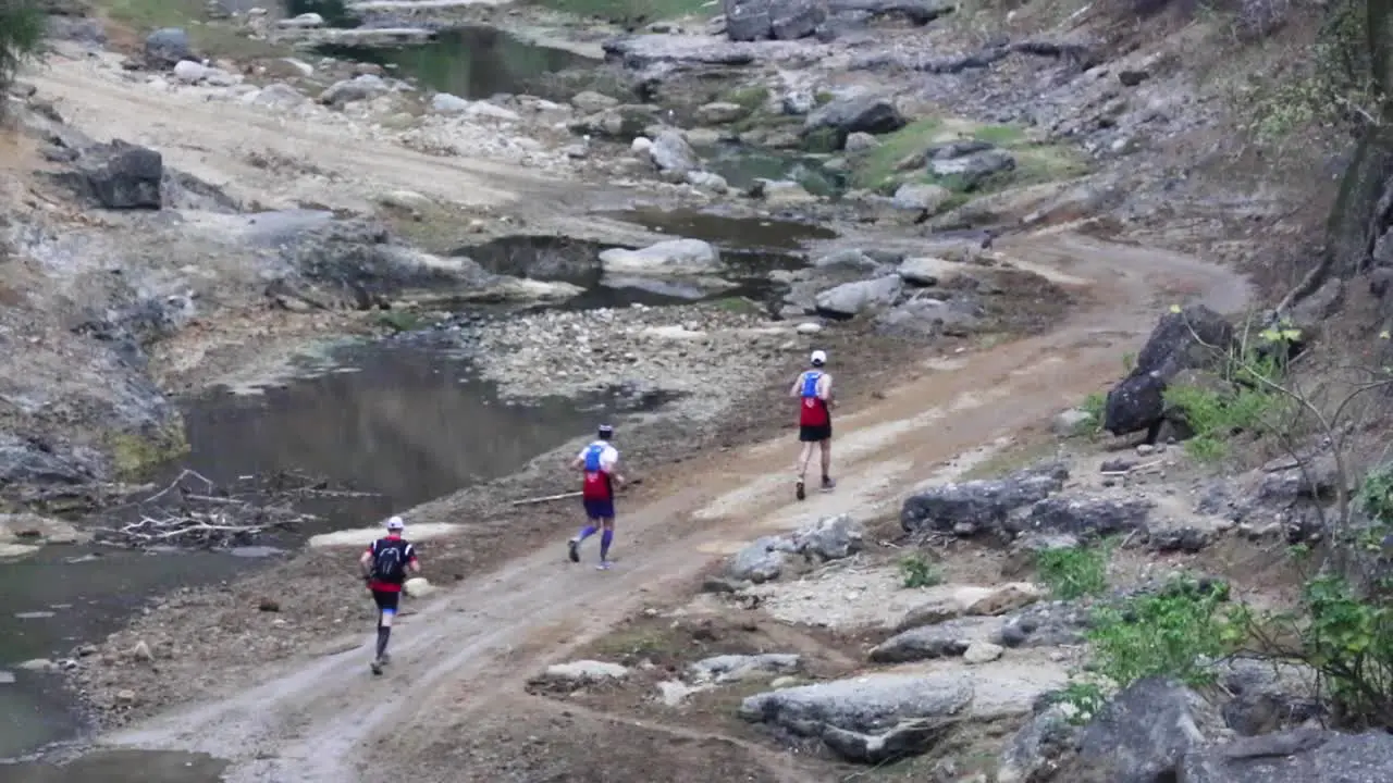 Group of marathon athletes running a charity race on dirt road along river creek through forest jungle in rural beautiful nature of Ecuador 50 fps