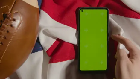 Overhead Studio Shot Of American Football On Stars And Stripes Flag With Person Using Green Screen Mobile Phone