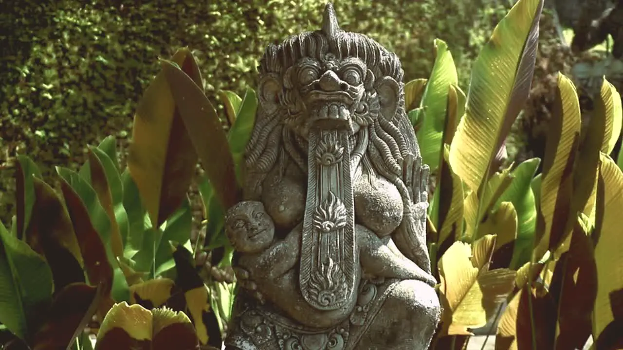 A beautiful balinese stone sculpture in front of green big leaves in a Temple of Ubud Bali Indonesia