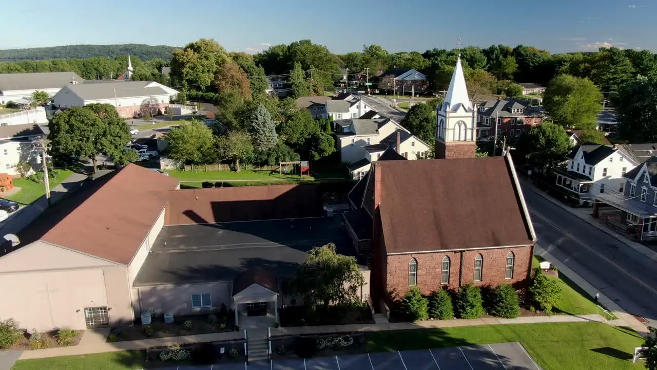 Establishing shot of old brown stone brick Lutheran Christian church in United States colonial historic homes line the street during summer aerial scene