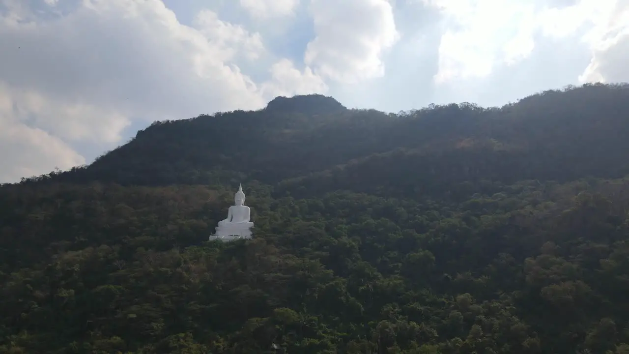 Luang Por Khao Wat Theppitak Punnaram sliding aerial footage to the left of the famous white Buddhist shrine on the mountain side revealing an afternoon summer sky and lovely changing colour trees