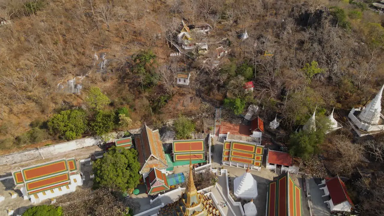 Wat Phra Phutthabat Saraburi Thailand reverse aerial footage of Buddhist structures within the forest with brown trees in summer also revealing the golden temple and complex road green trees