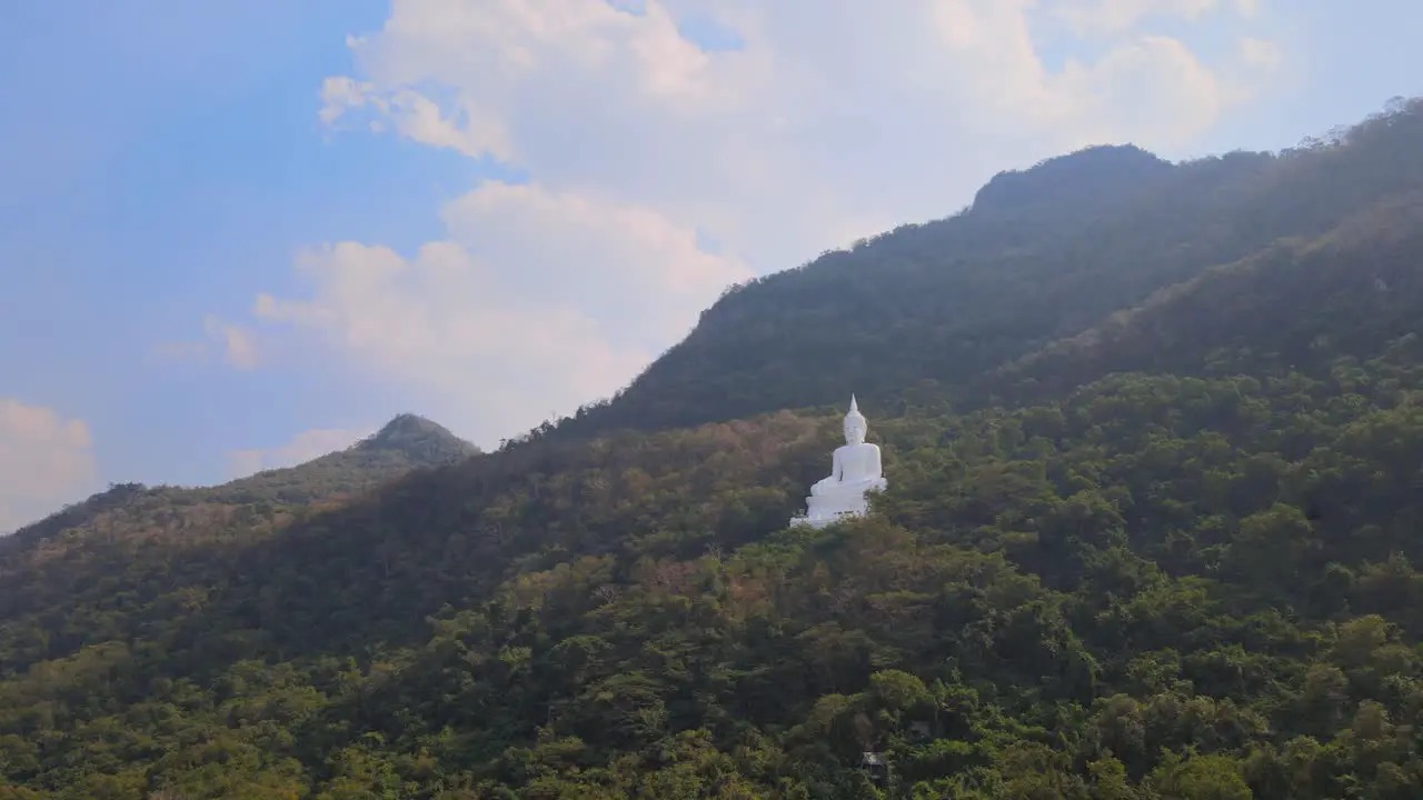 Luang Por Khao Wat Theppitak Punnaram aerial 4K footage towards the giant White Buddha statue on a mountain side in Pak Chong Thailand in the afternoon blue cloudy sky birds flying around