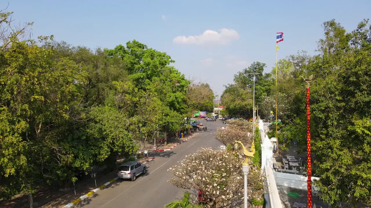 Wat Phra Phutthabat Saraburi Thailand a steady aerial 4K footage of a community entrance into the Buddhist temple a Thai flag street lights people crossing cars and motorcycles passing