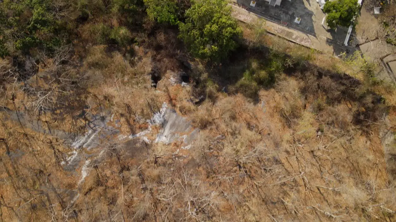 Wat Phra Phutthabat Saraburi Thailand 4k aerial footage from above the dry and brown forest during summer towards the temple complex road on the right green trees at the garden