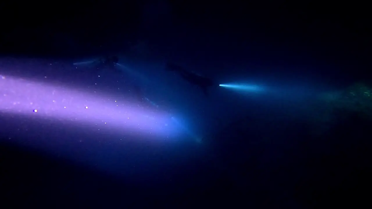 Scuba divers with torches on the bottom of an underwater cave